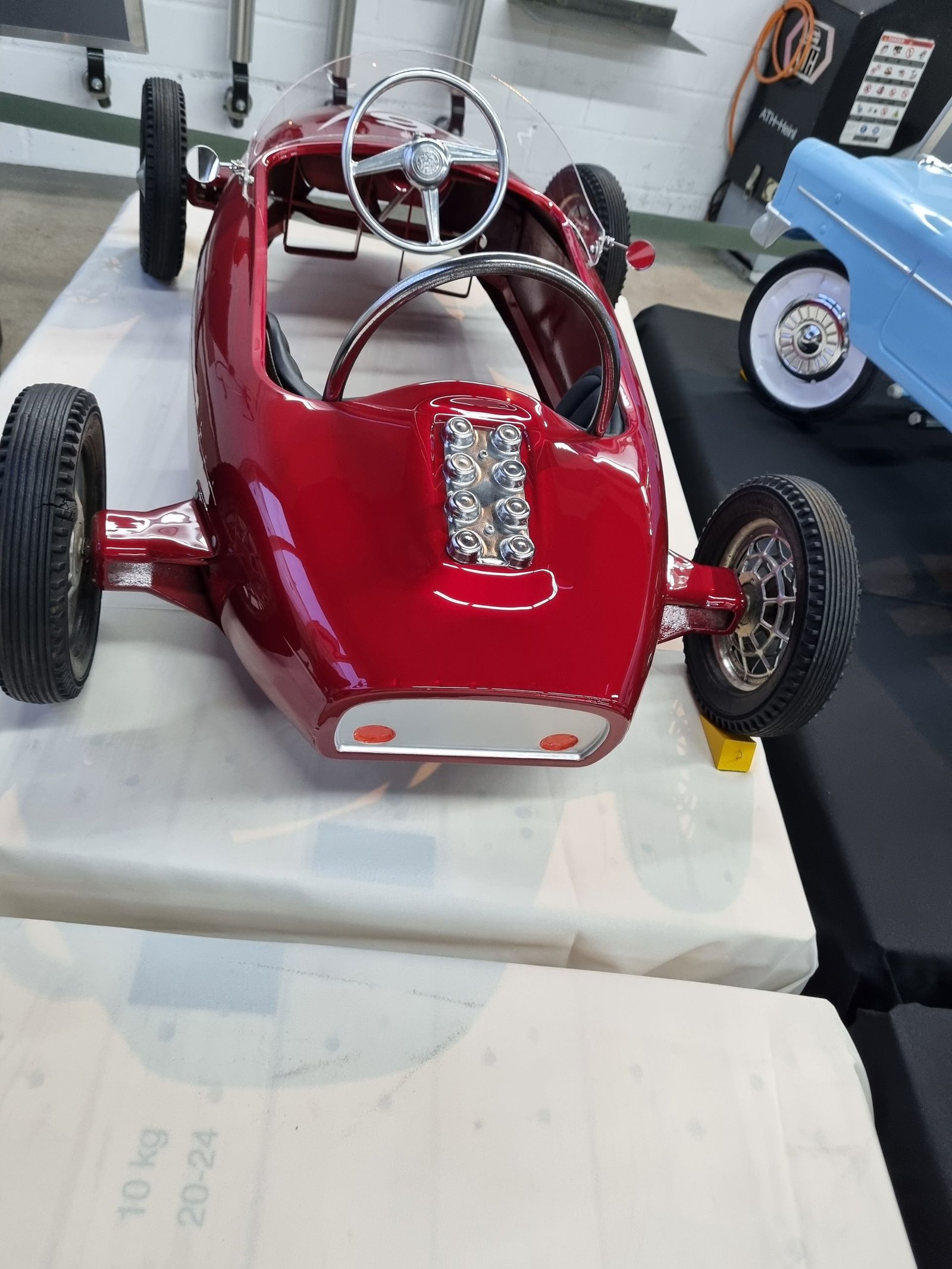 Ein rotes Tretauto steht auf einem weißen Tisch